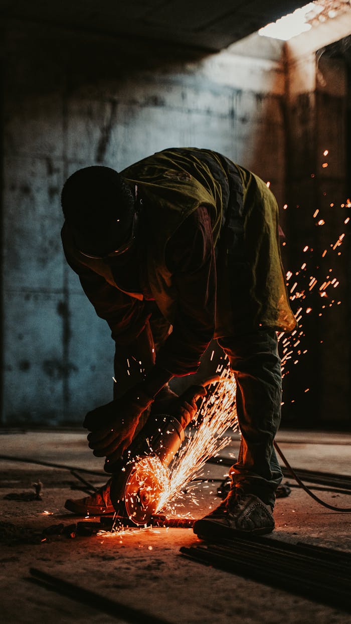 About Worker in silhouette cutting metal with sparks in a construction site at sunset.
